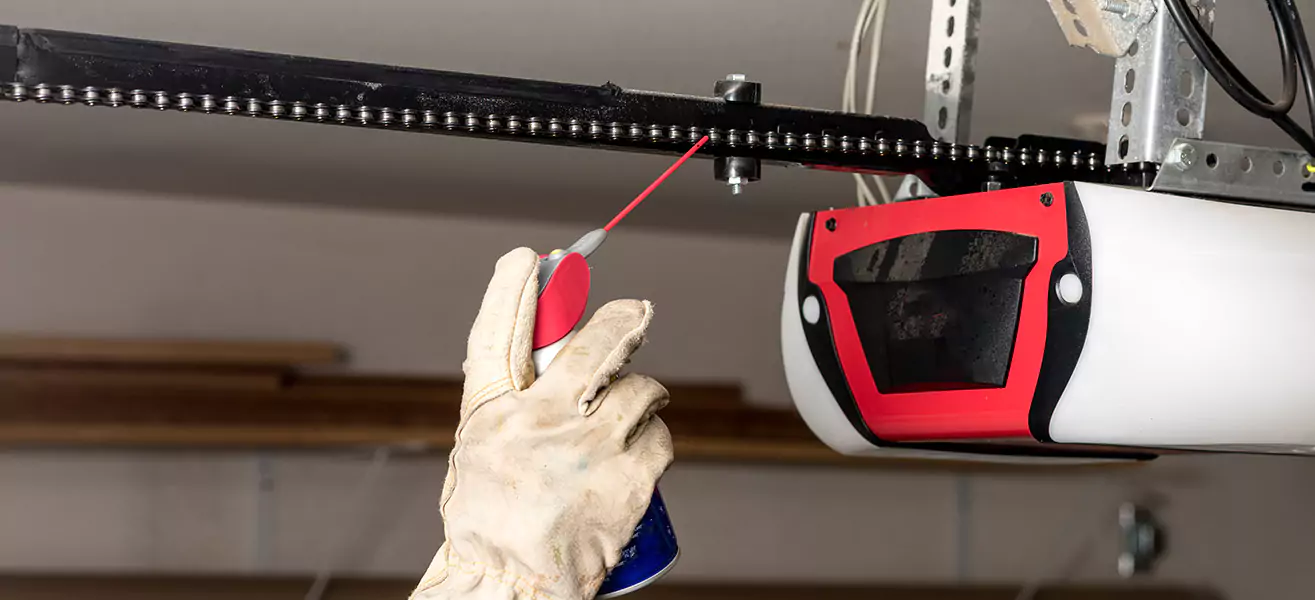 Garage door professional lubricating a chain garage door opener.