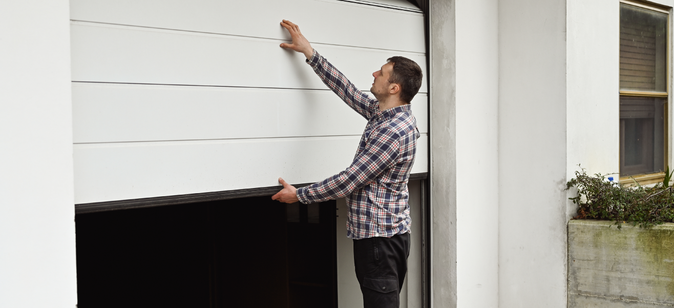 Man standing outside holding up a crooked garage door