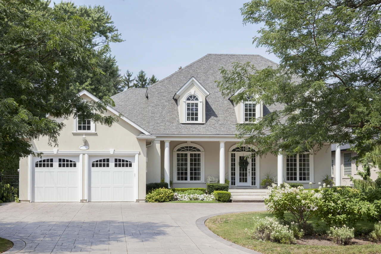 A gray house with trees and white garage doors.