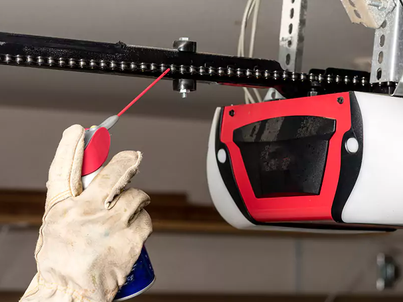 Garage door professional lubricating a chain garage door opener.