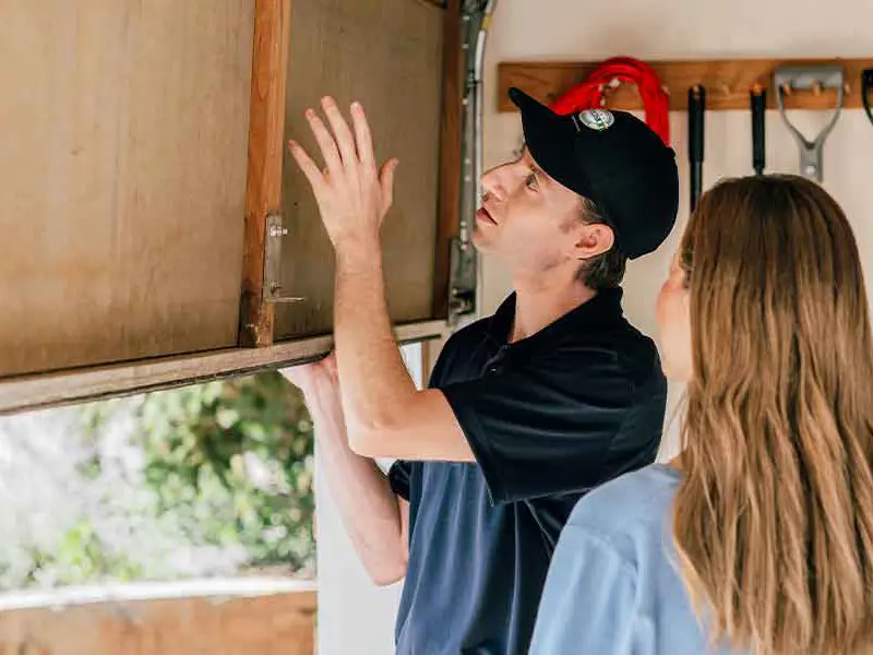 A Precision Garage Door Service professional examining a garage door with a customer.
