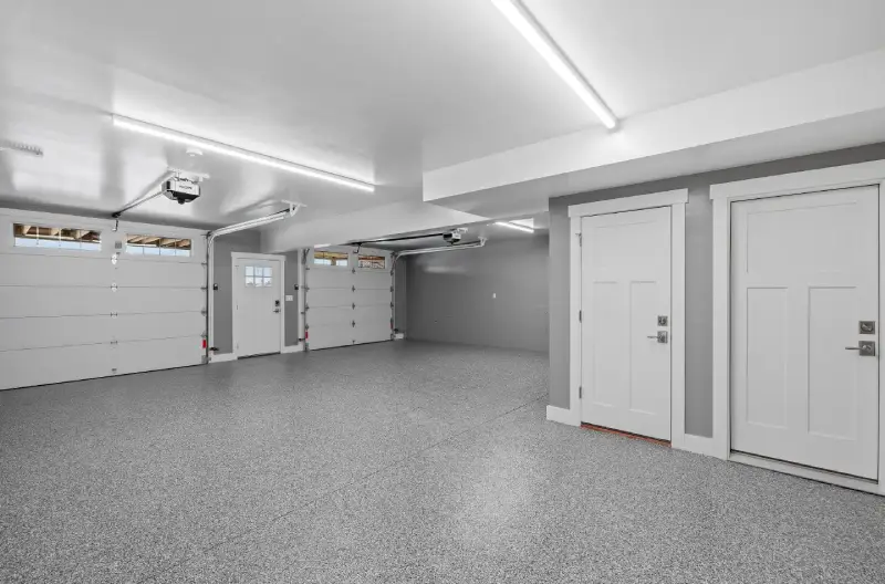 A remodeled garage with gray flooring, white doors and ceilings, and new light fixtures.