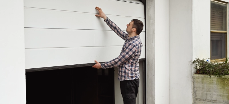 Man standing outside holding up a crooked garage door.