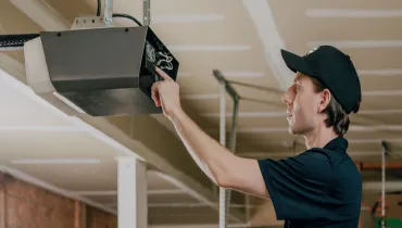 A Precision Garage Door service professional examines garage door opener with blinking lights.